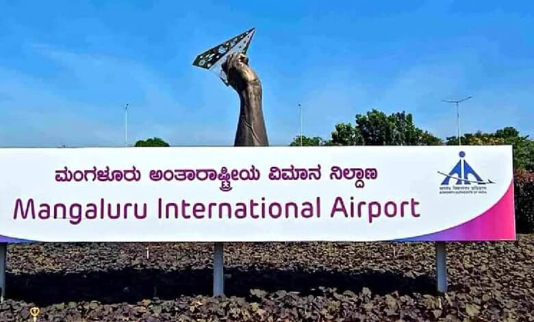 Mangaluru International Airport sign with a sculpture of a hand holding a satellite dish.