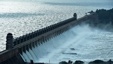 Dam releasing water into the river with mist and trees in the background.