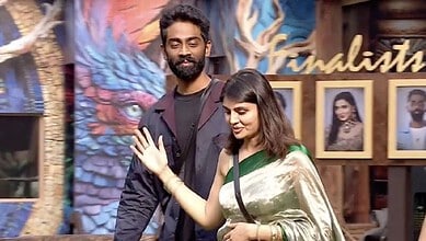 A woman in a green saree and a man with a beard and dark hair waving at the camera at an event.