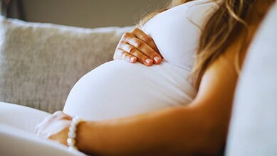 Pregnant woman resting her hand on her belly on a sofa.