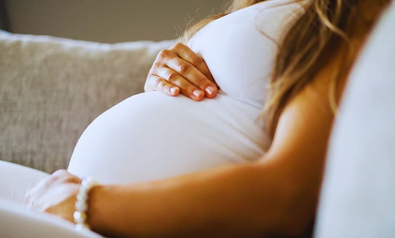 Pregnant woman resting her hand on her belly on a sofa.