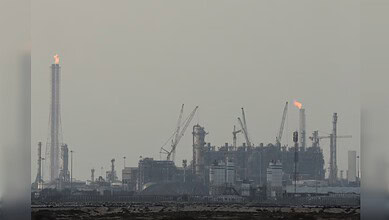 Industrial gas plant with smoke and flames, cranes, and industrial structures in Qatar.