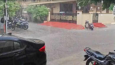 Flooded street with parked motorcycles and cars during heavy rain in an urban area.