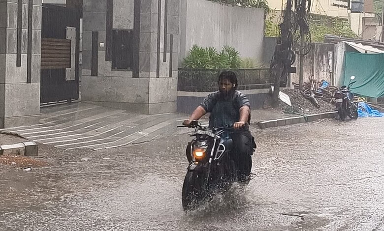 Motorcyclist navigating through flooded street during heavy rain in an urban setting.