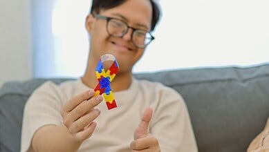 Happy person holding a colourful puzzle piece, smiling at home.