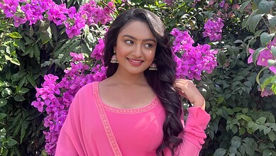 A woman in a pink traditional dress standing among vibrant purple bougainvillaea flowers.