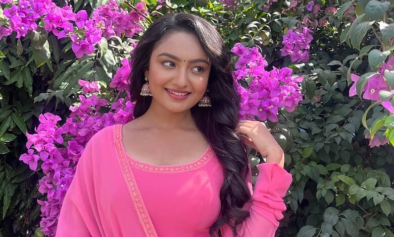 A woman in a pink traditional dress standing among vibrant purple bougainvillaea flowers.