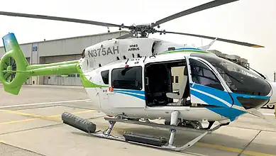 A sleek helicopter with blue and green accents parked on the airport runway.