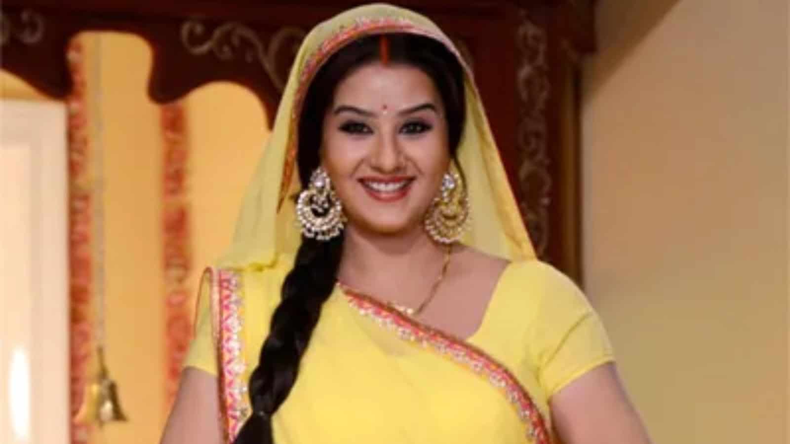 A woman in traditional yellow attire with jewelry, smiling in an indoor setting.