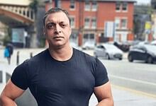 Portrait of a man in a black t-shirt standing outdoors in an urban setting.