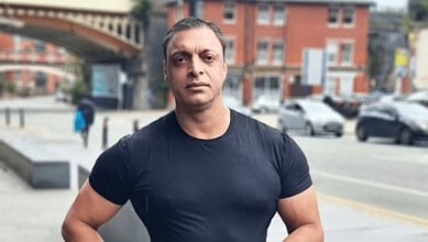 Portrait of a man in a black t-shirt standing outdoors in an urban setting.
