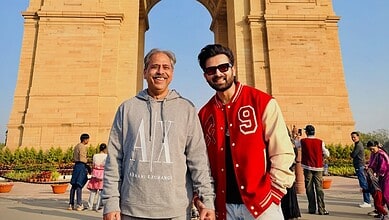 Two men smiling in front of India Gate, Delhi, during daytime with tourists around.