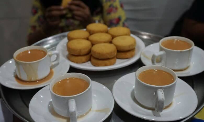 Tea cups with saucers and a plate of cookies on a tray, with a person in the background.