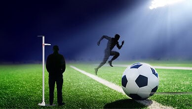 Silhouette of a soccer player jumping to score a goal during a match at night.