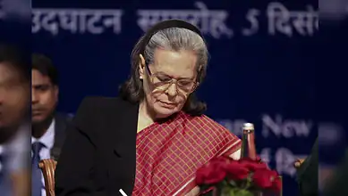 Sonia Gandhi attends an event while looking down at documents on stage.