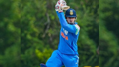 Indian cricketer batting in a T20I match, wearing blue jersey and helmet, with green background.