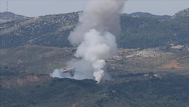 Volcanic eruption with smoke rising from a mountain in a hilly landscape.