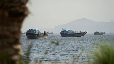 Ships anchored on calm waters with a distant mountain in the background.