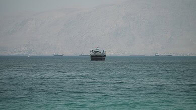 Large ships sailing through the Strait of Hormuz with mountainous background.