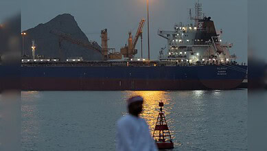 Man seated by Muscat waterfront as cargo vessel anchors at Sultan Qaboos Port amid Gulf tensions