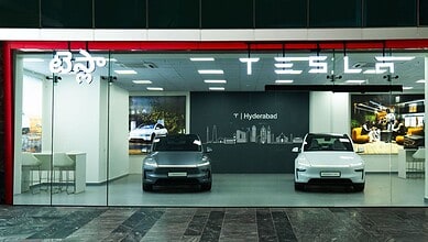Tesla showroom displaying two electric cars inside with a modern interior and branding.