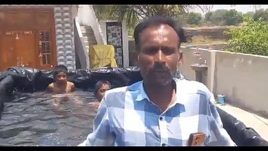 Village man outdoors near water with children swimming in the background.