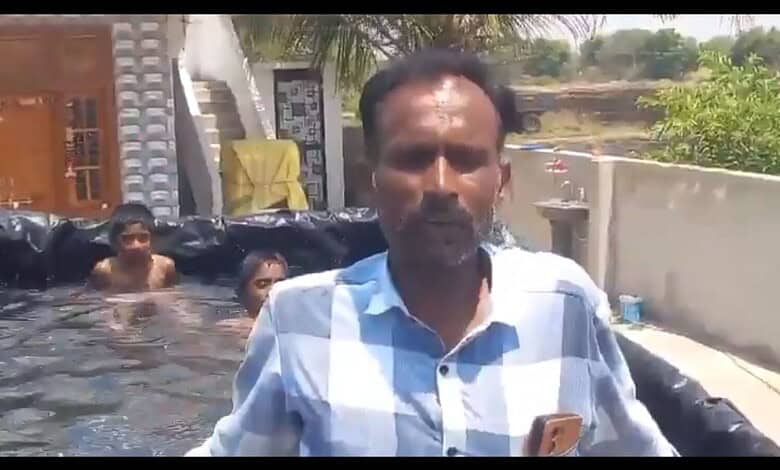 Village man outdoors near water with children swimming in the background.