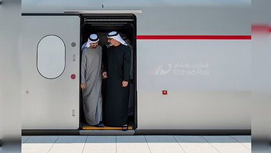 Two men in traditional UAE attire disembark from Etihad Rail train in UAE.