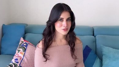 Uorfi Javed with long dark hair, wearing a pink top, sitting on a blue sofa.