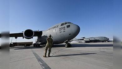Military personnel inspecting a large US Air Force cargo plane on the tarmac.