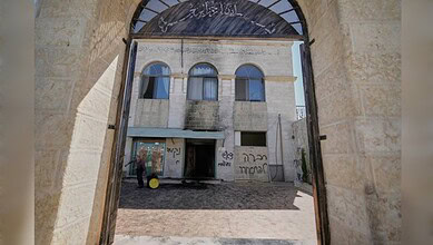 View through an arched stone gateway showing a historic building with graffiti on its walls.