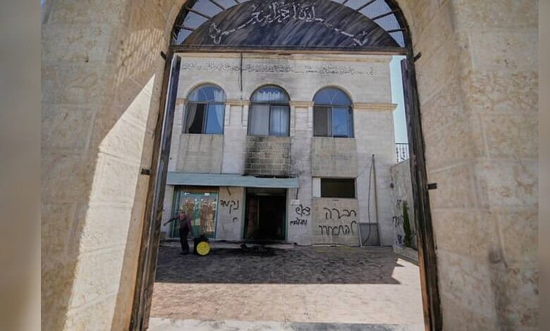 View through an arched stone gateway showing a historic building with graffiti on its walls.