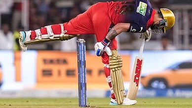 Cricket player in red uniform diving to catch the ball during a match.