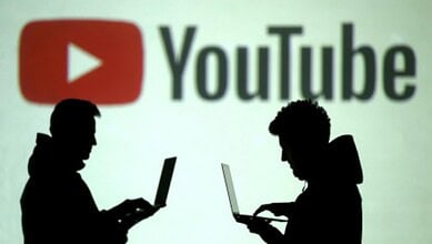 Silhouettes of two people using laptops in front of a large YouTube logo, representing online content and digital platforms.