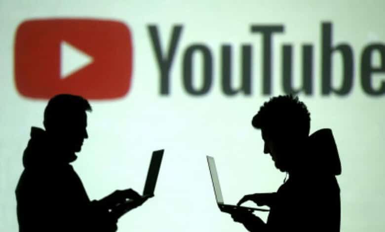 Silhouettes of two people using laptops in front of a large YouTube logo, representing online content and digital platforms.