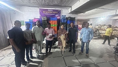 Group of people standing in Zepto warehouse with expired food items in the background.