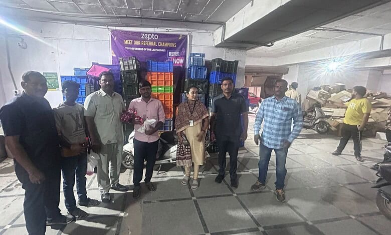 Group of people standing in Zepto warehouse with expired food items in the background.