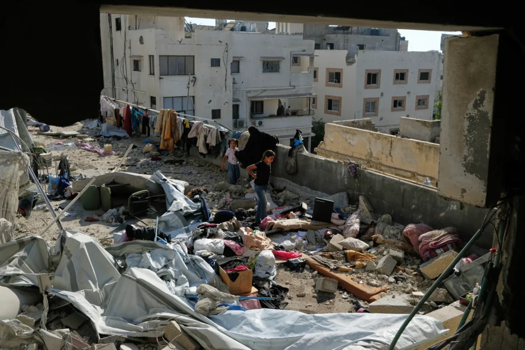 People amid destruction and debris on a damaged building rooftop in Gaza.