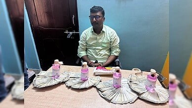 Man sitting at a table with stacks of money and water bottles in front of him.