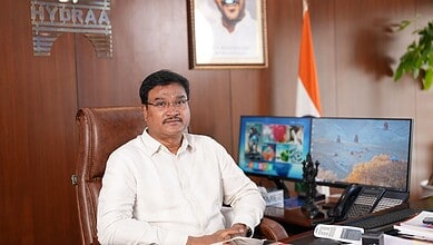 Official portrait of a man in a white shirt sitting at a desk in an office.