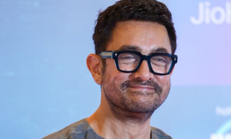 Aamir Khan at a public event, smiling with glasses and a beard.