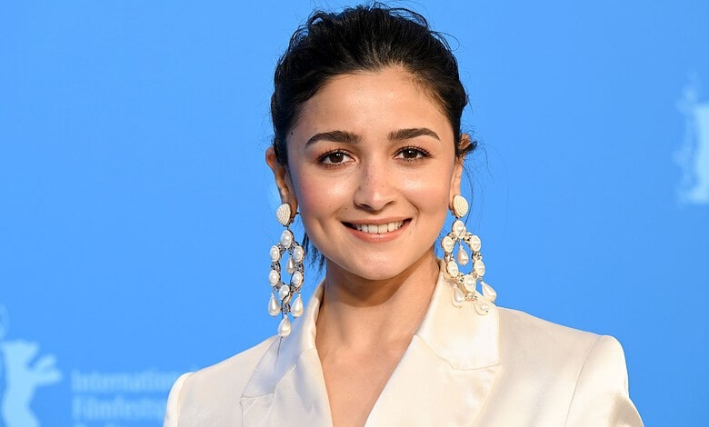 Alia Bhatt smiling at an event with a blue background and white logo.