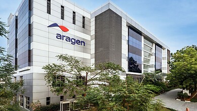 Modern Aragen biotech building with glass windows and logo, surrounded by greenery in an urban setting.