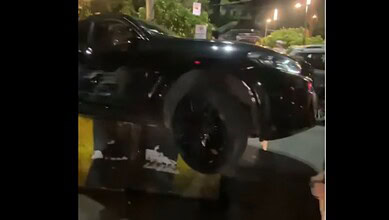 Black BMW mounting a divider on Hyderabad's KBR Park road at night.