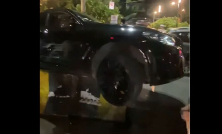 Black BMW mounting a divider on Hyderabad's KBR Park road at night.
