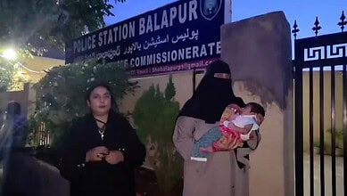 Woman holding a newborn outside Hyderabad's Balapur police station at night.