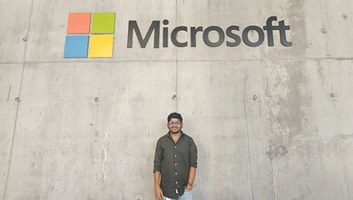 Person standing in front of a concrete wall with Microsoft logo in the background.
