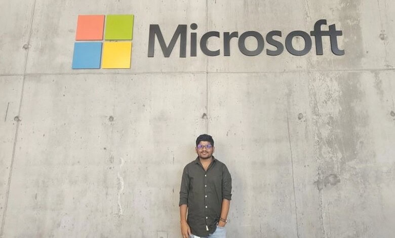 Person standing in front of a concrete wall with Microsoft logo in the background.