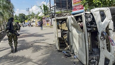Upside-down white vehicle on a street with a police officer nearby during a protest.