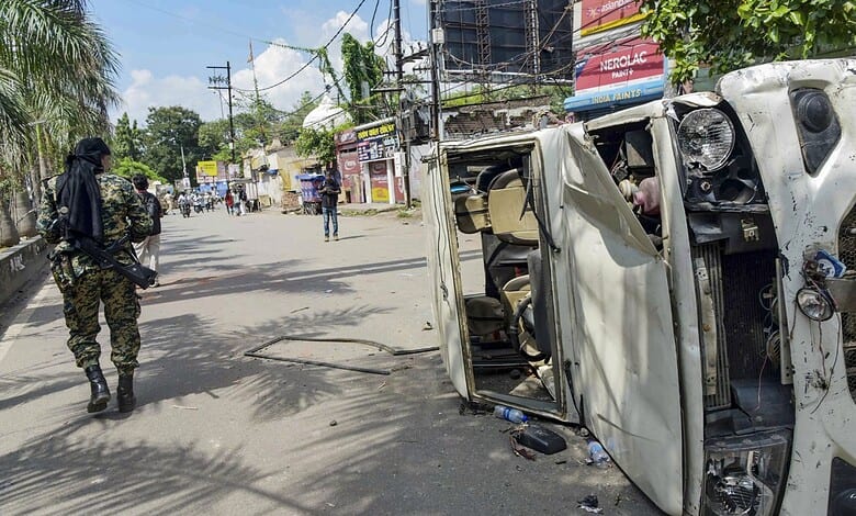 Upside-down white vehicle on a street with a police officer nearby during a protest.